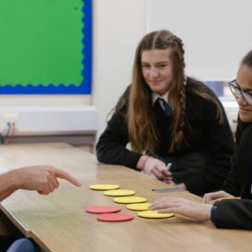 A teacher pointing at counters with three pupils sat at a table