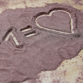 Image of the equation one plus one equals heart, drawn in the sand