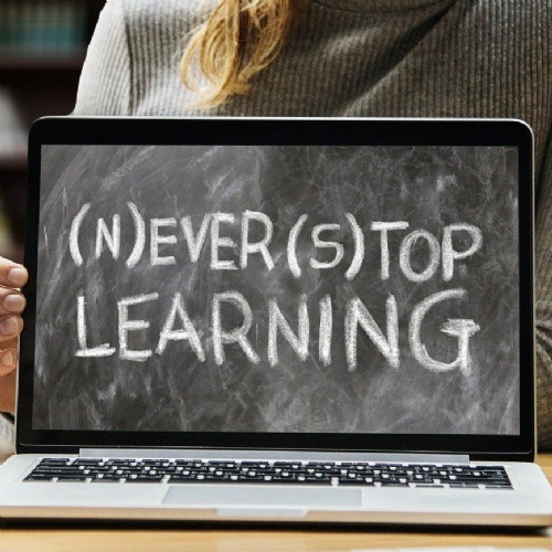 Person holding laptop displaying the words Never Stop Learning and Ever Top Learning