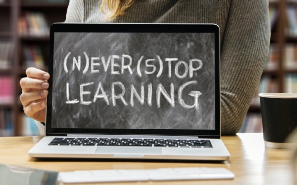 Person holding laptop displaying the words Never Stop Learning and Ever Top Learning